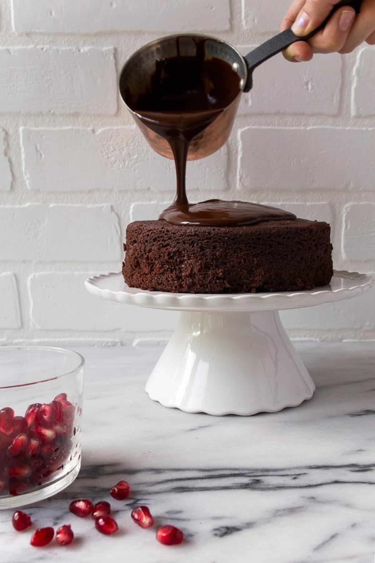 Hand pouring warm melted chocolate on top of a cake stand.