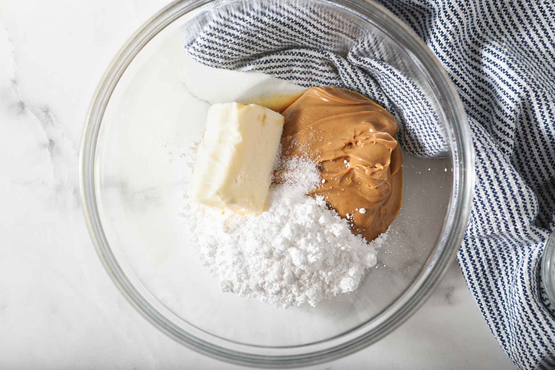 Butter, peanut butter, and powdered sugar in a clear glass bowl.