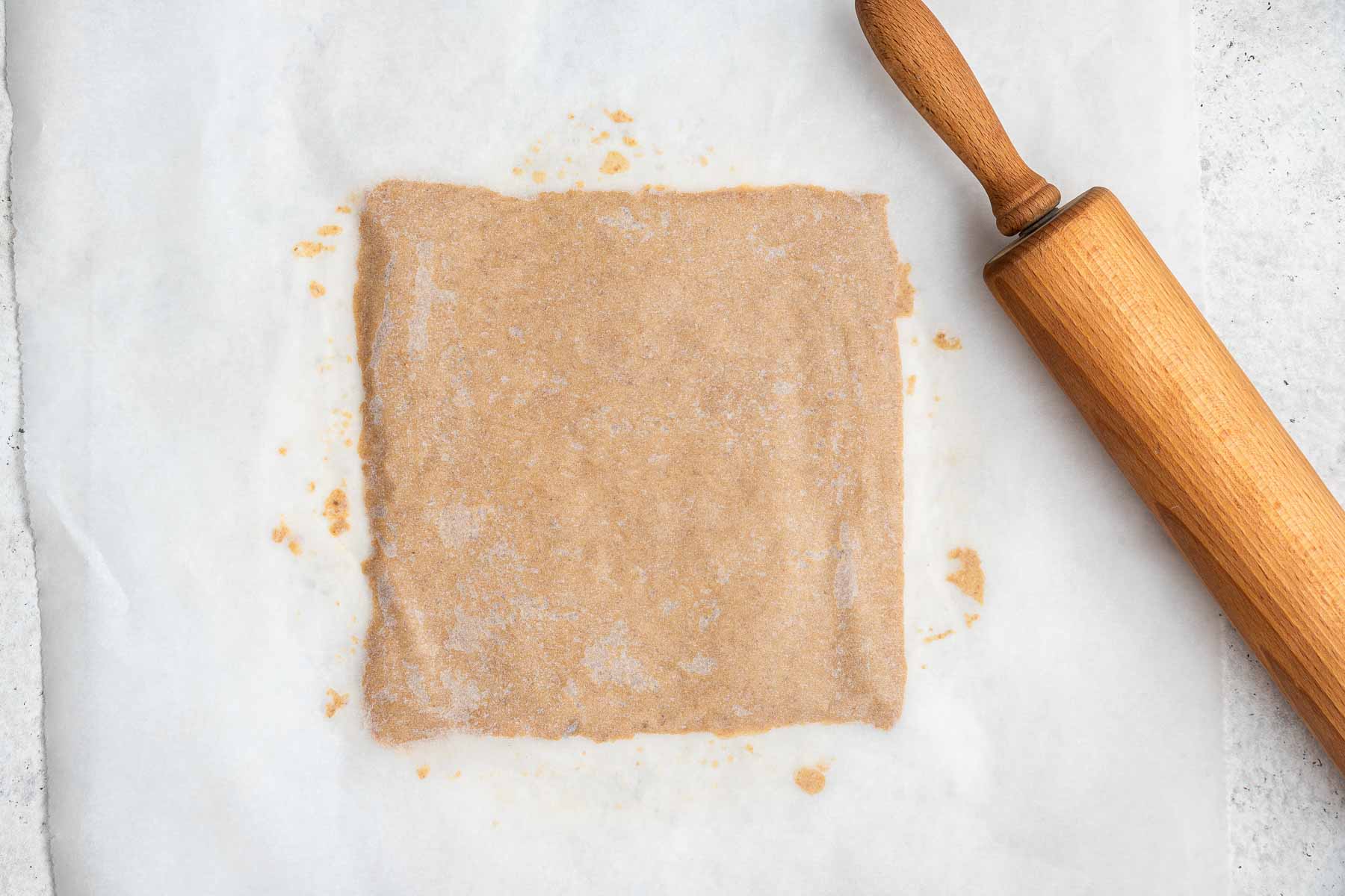 Dough rolled to a perfect square with rolling pin on the side.