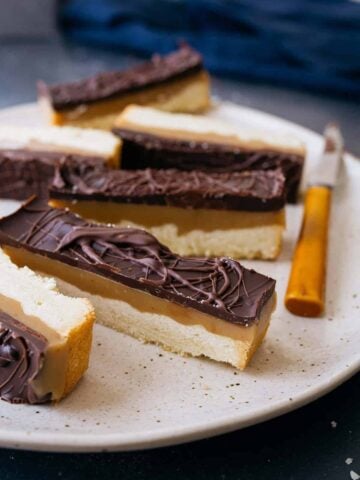 Homemade Twix bars on a plate with knife on side.