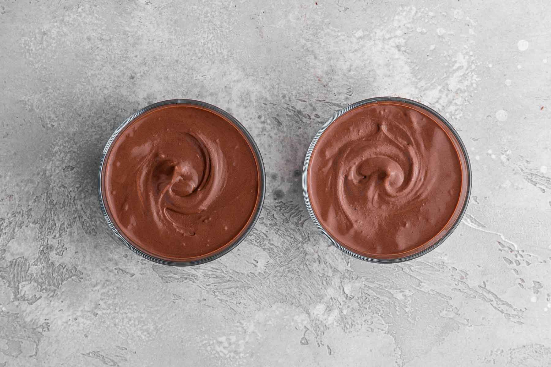 Two round mason jars full of chocolate mousse on grey counter.