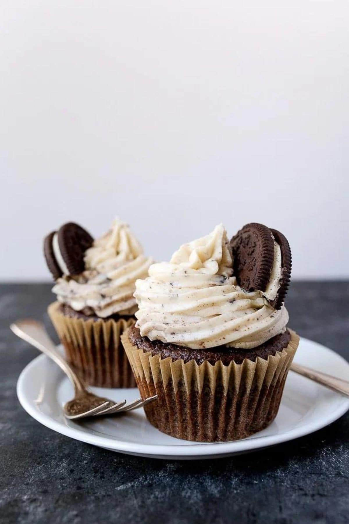 Two chocolate cupcakes with white icing and a cookie on top.