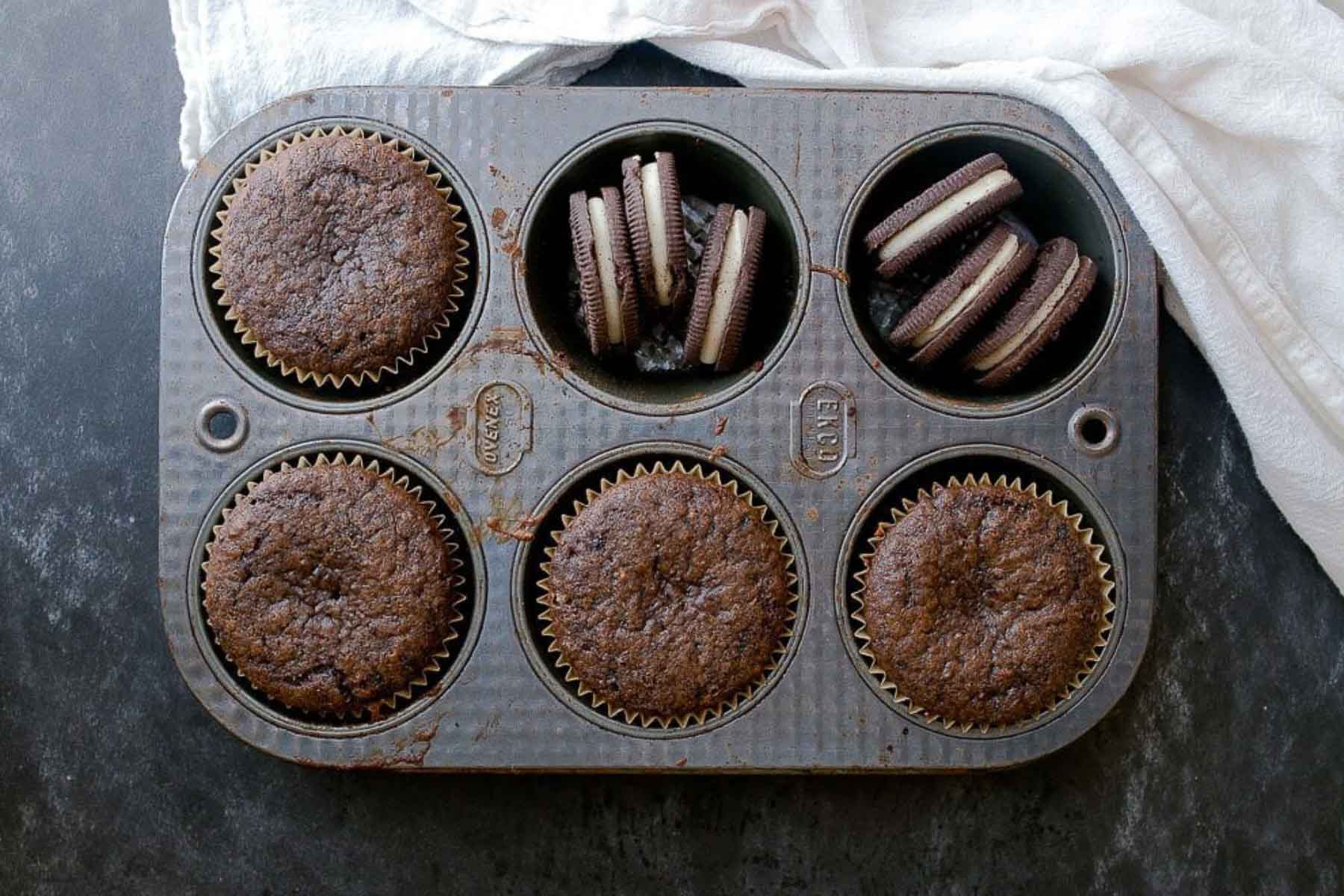 Four chocolate cupcakes in a pan with Oreo cookies in the other holes.