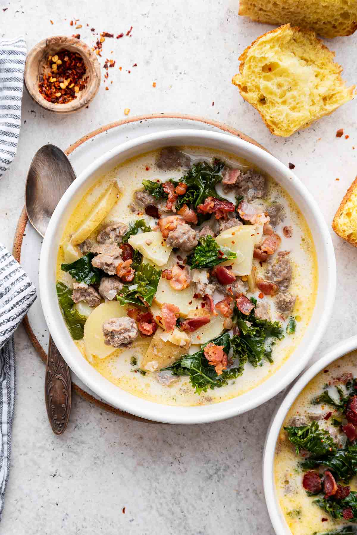 Overhead image of two bowls of chunky white sauce with kale, bacon, and potatoes.