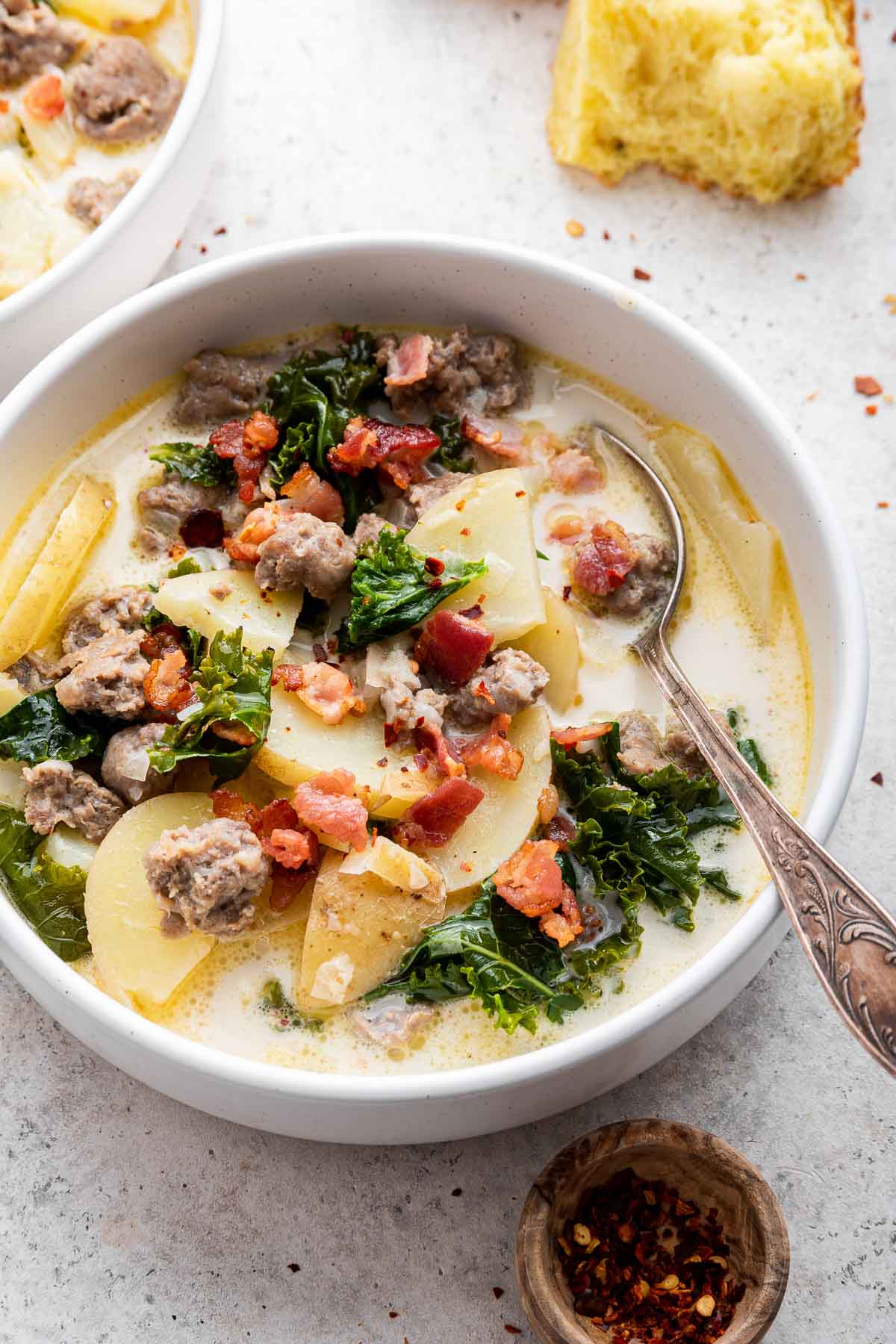 Vertical image of white creamy stew with potatoes, sausage, bacon crumbles and kale.
