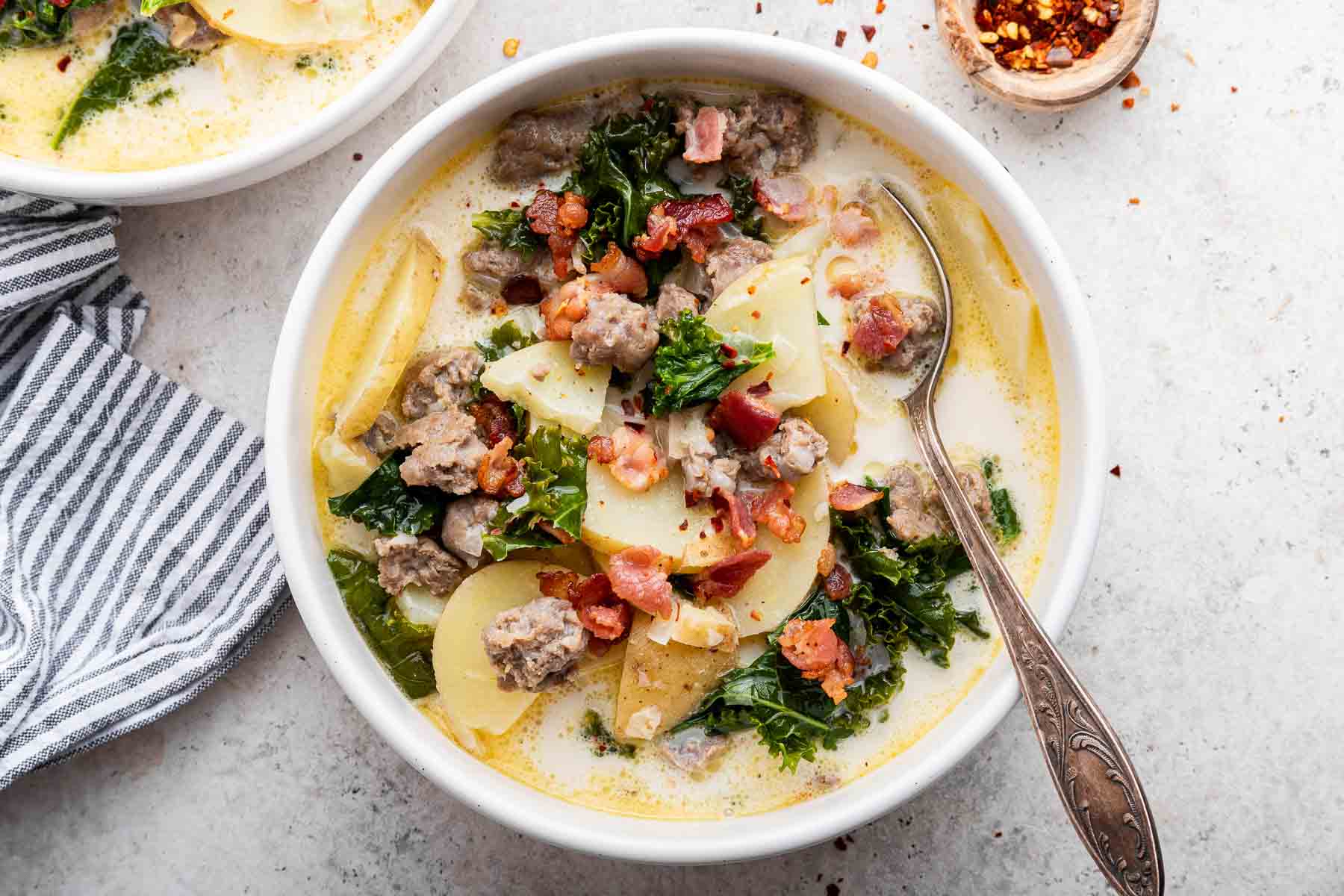 Horizontal image of zuppa toscana, a potato sausage soup with bacon and kale on top.