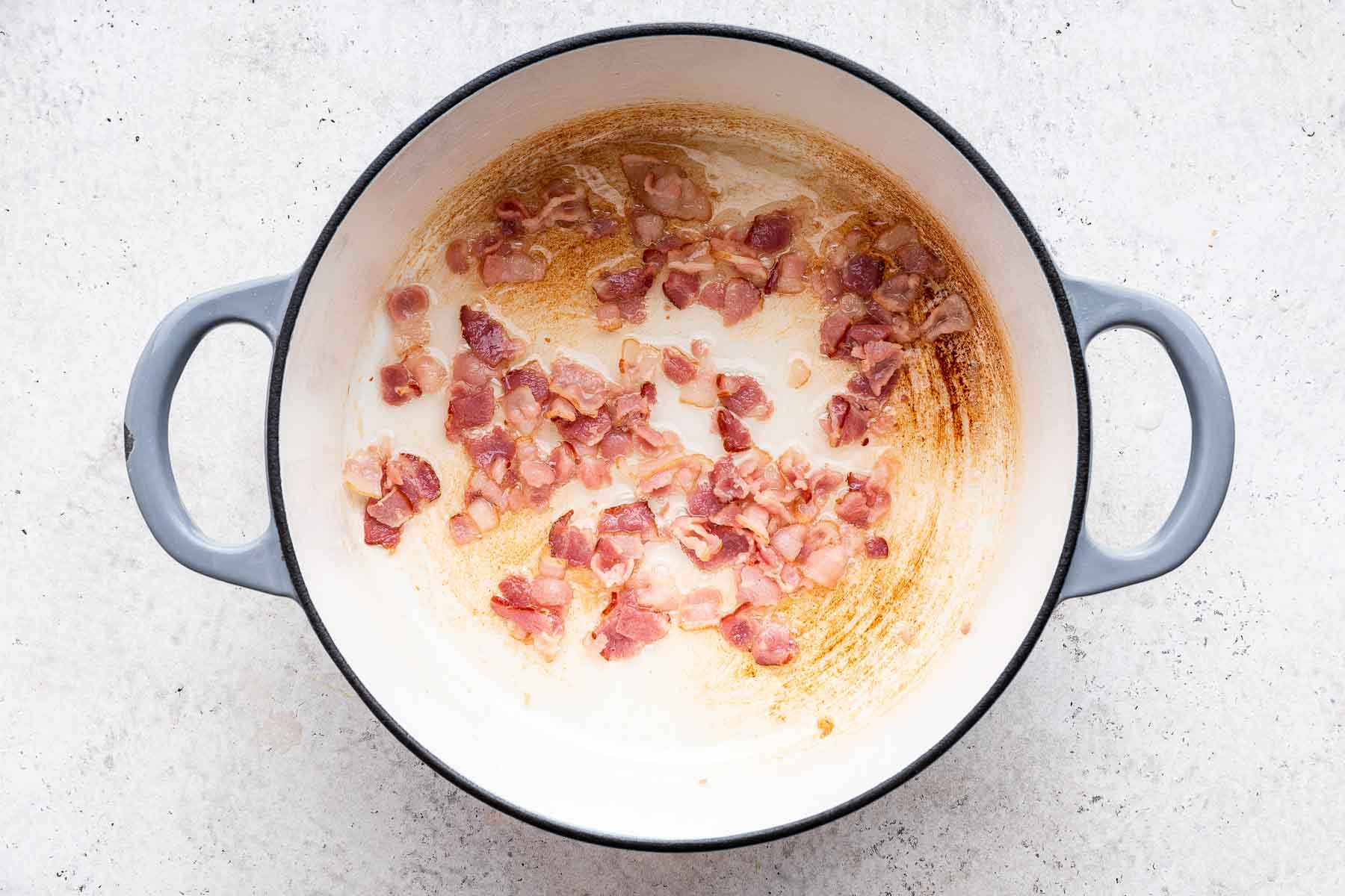 Chopped bacon cooking in white pan.
