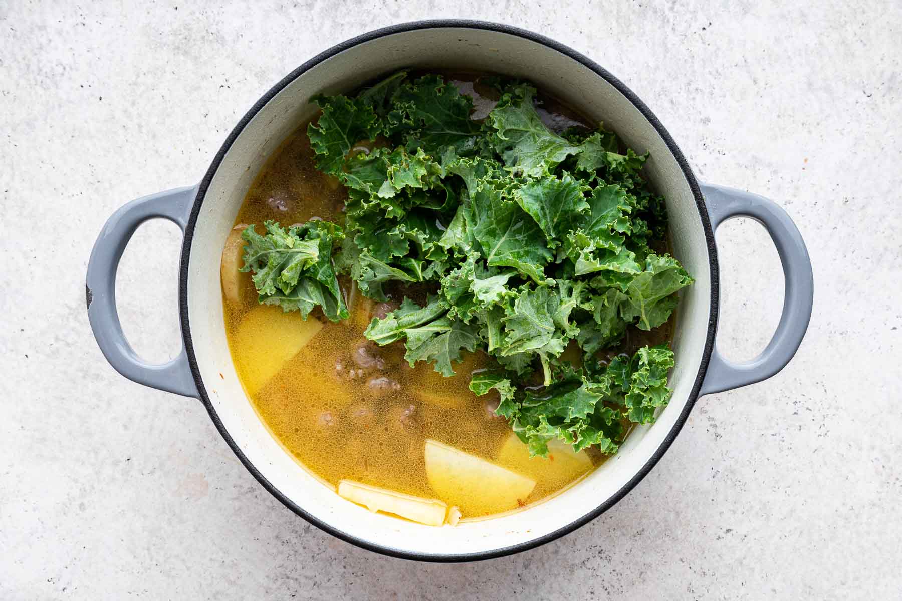 Adding kale to zuppa toscana soup on stove.