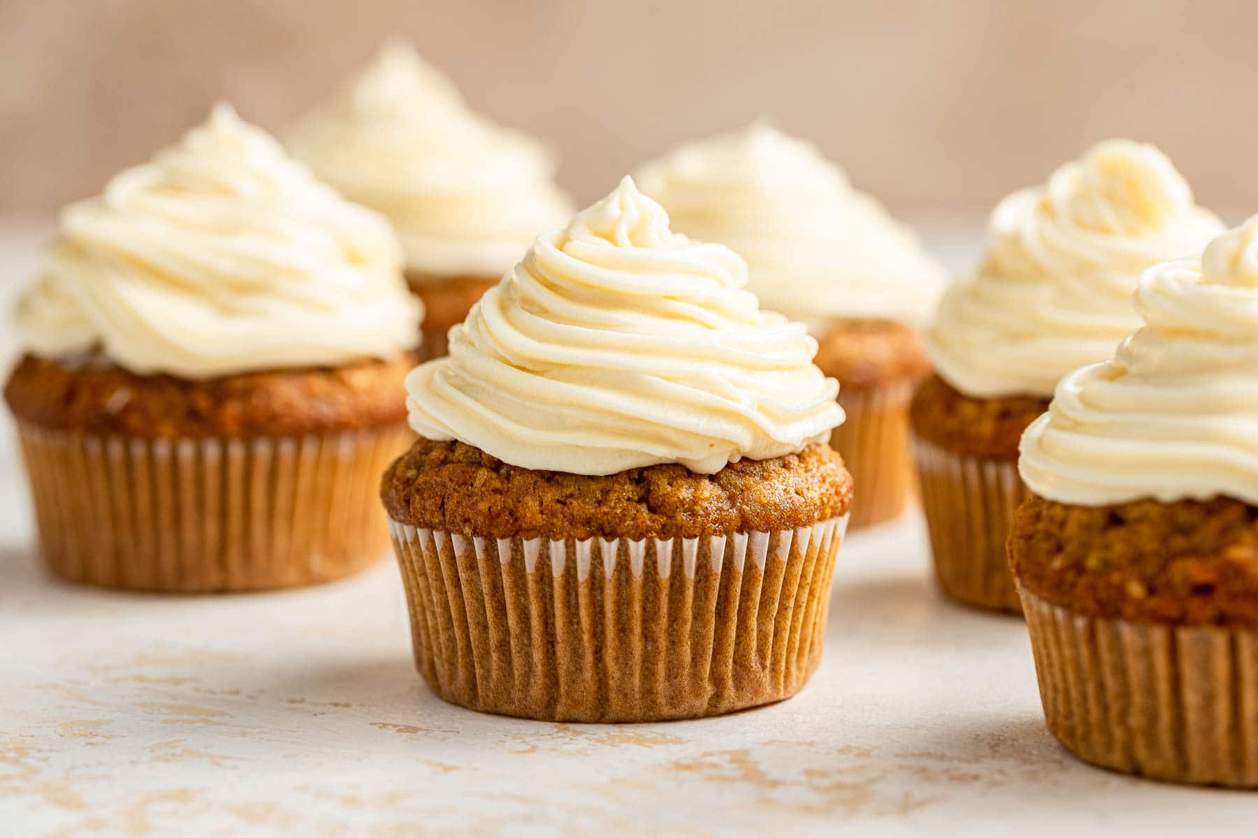 Six frosted carrot cake cupcakes with white frosting.