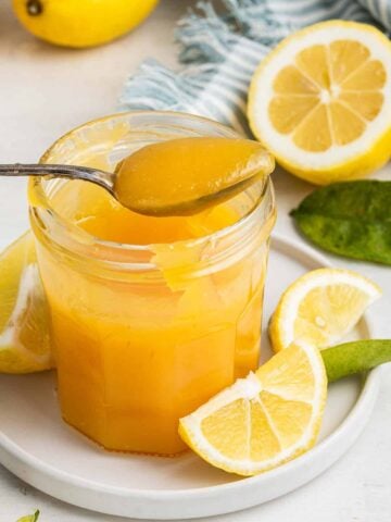 Glass jar of microwave lemon curd with spoon removing a scoop.