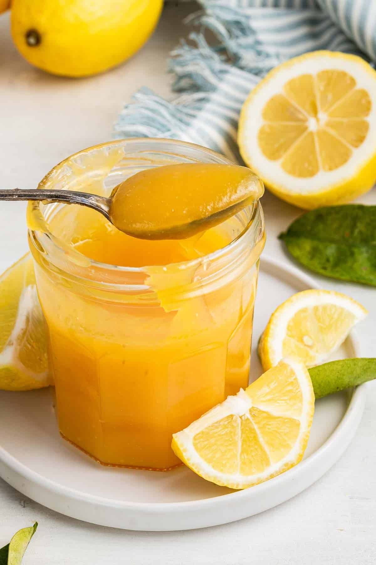 Glass jar of microwave lemon curd with spoon removing a scoop.
