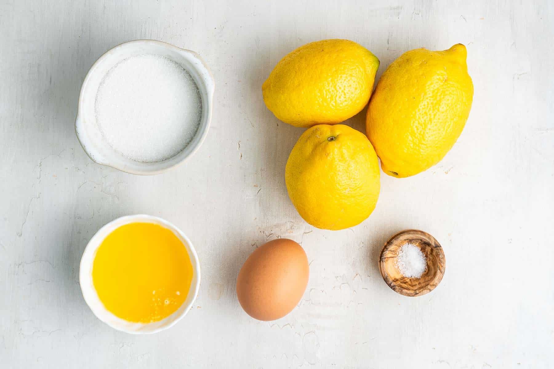 Three lemons, egg, butter and sugar on marble counter.