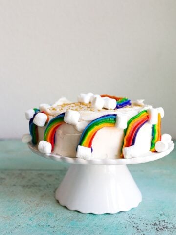 Rainbow Cake Recipe: mini rainbow cake with rainbow buttercream, marshmallow clouds and gold sprinkles. Perfect first birthday cake or rainbow baby smash cake.