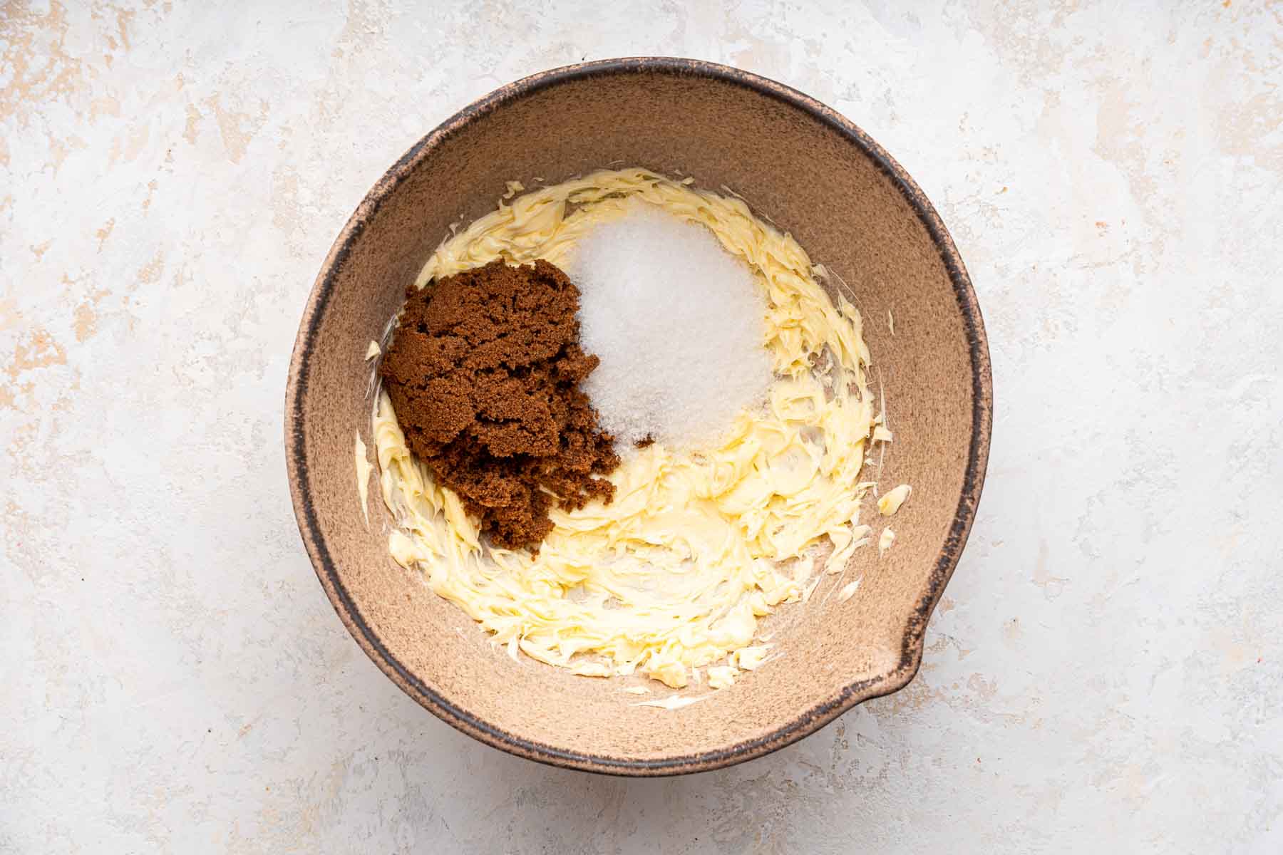 Brown bowl with beaten yellow butter, white sugar and brown sugar on top.