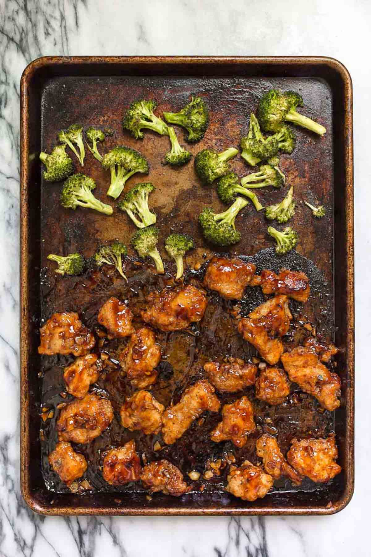 Dark metal sheet pan with honey garlic chicken thighs pieces and broccoli after cooking.