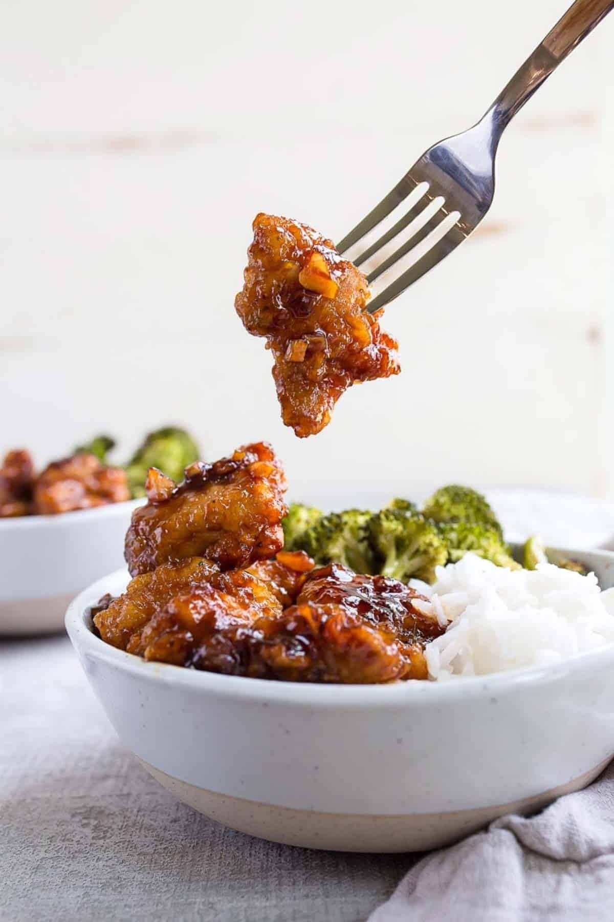 Fork removing a golden brown piece of food from a bowl with rice and broccoli.