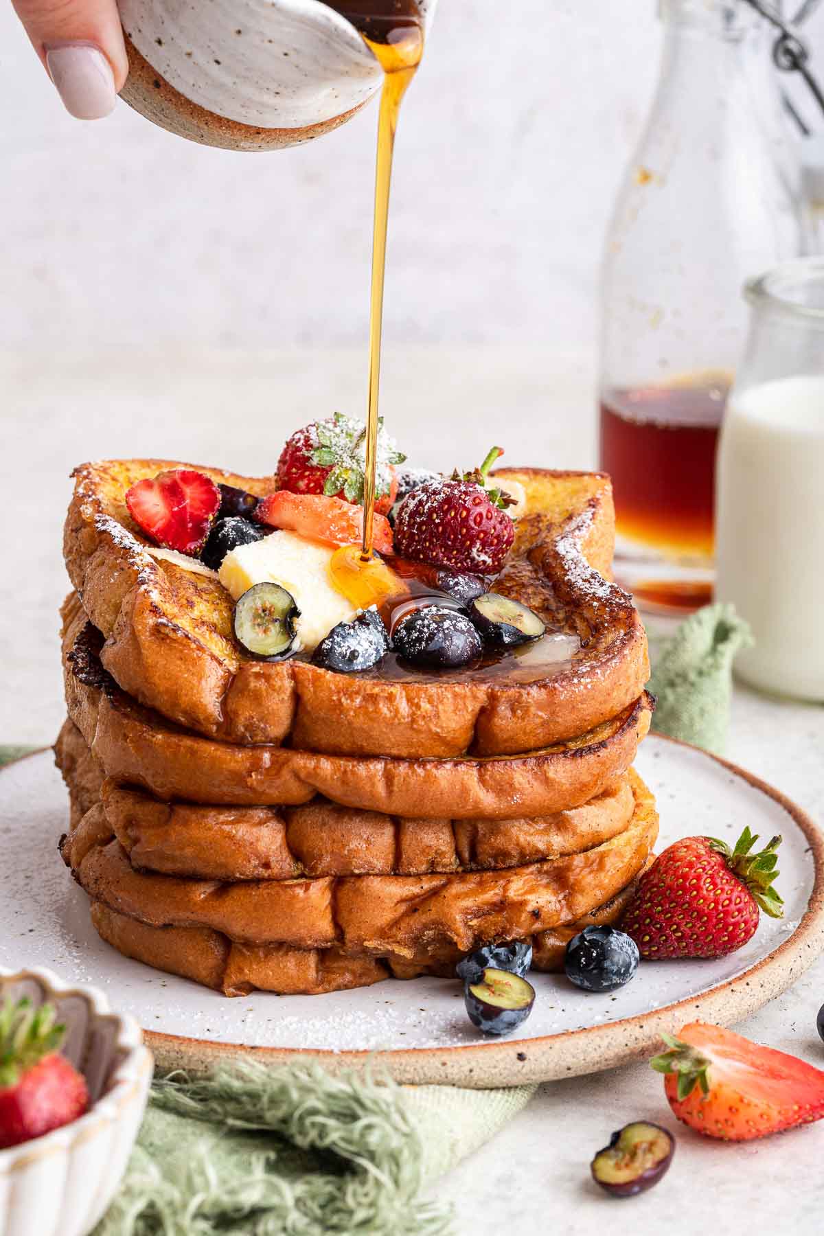 Stack of brioche French toast with berries and syrup pouring over the top.