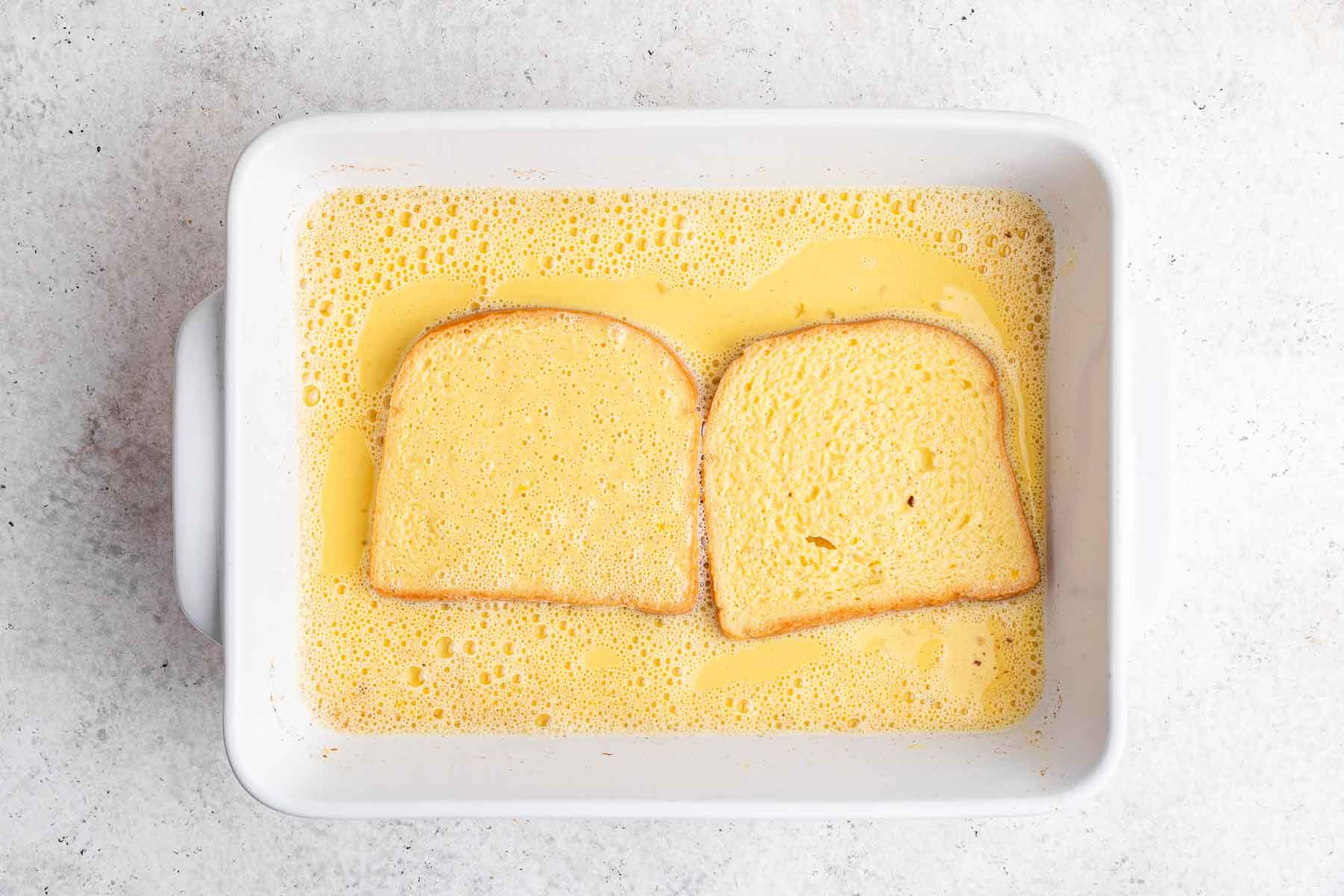 Two slices of bread soaking in yellow egg custard.