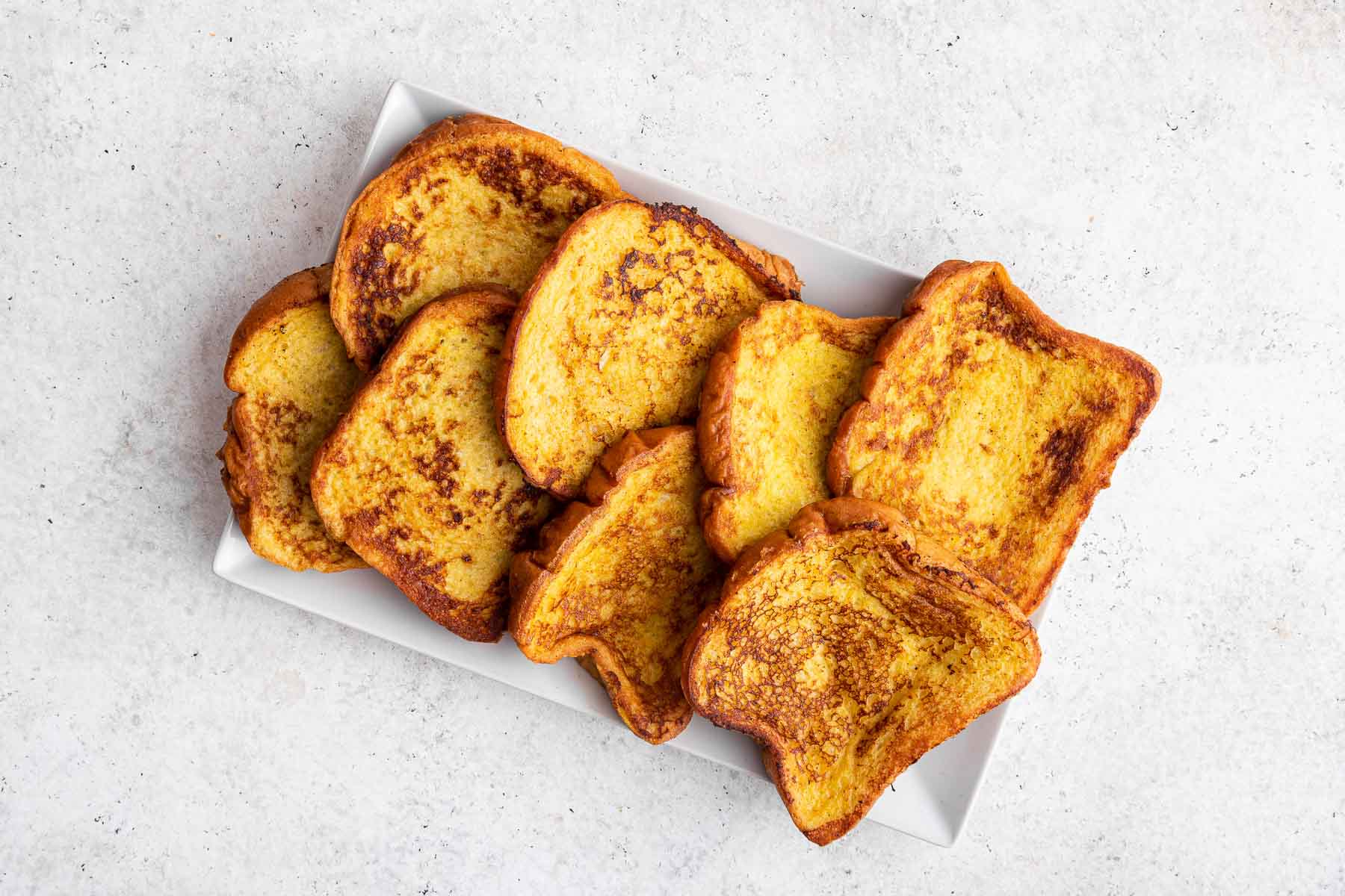 Brioche French toast bread slices stacked on rectangular white plate.