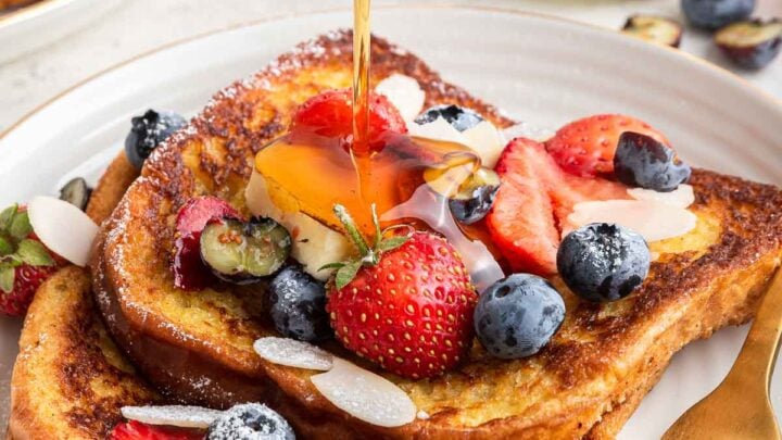 Brioche French toast for two on plate with fresh berries and syrup being poured on top.