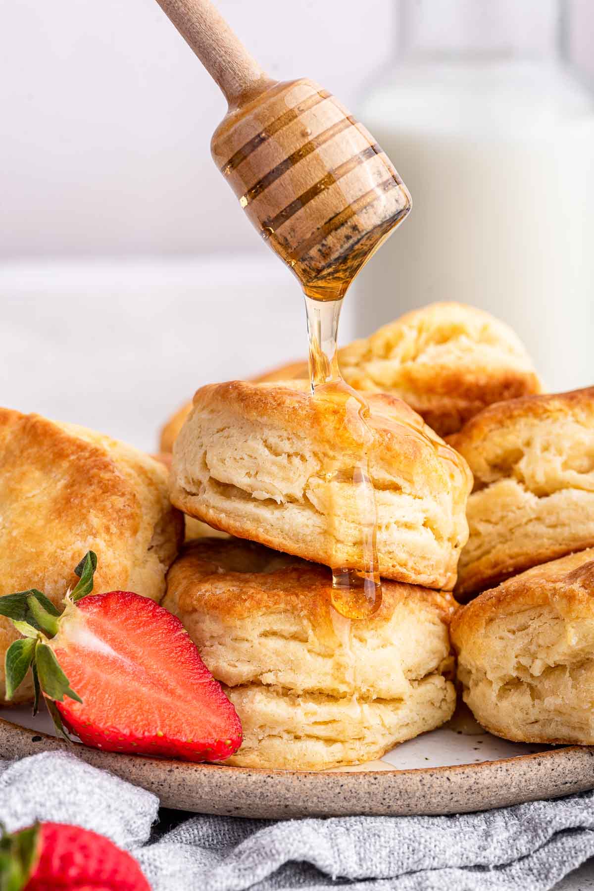 Honey dipper drizzling honey on stack of freshly baked buttermilk biscuits.