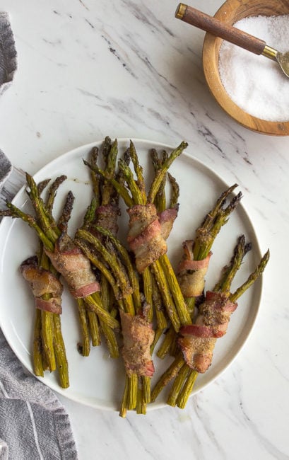 Bacon wrapped asparagus spears on white plate.