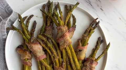 Bacon wrapped asparagus spears on white plate.