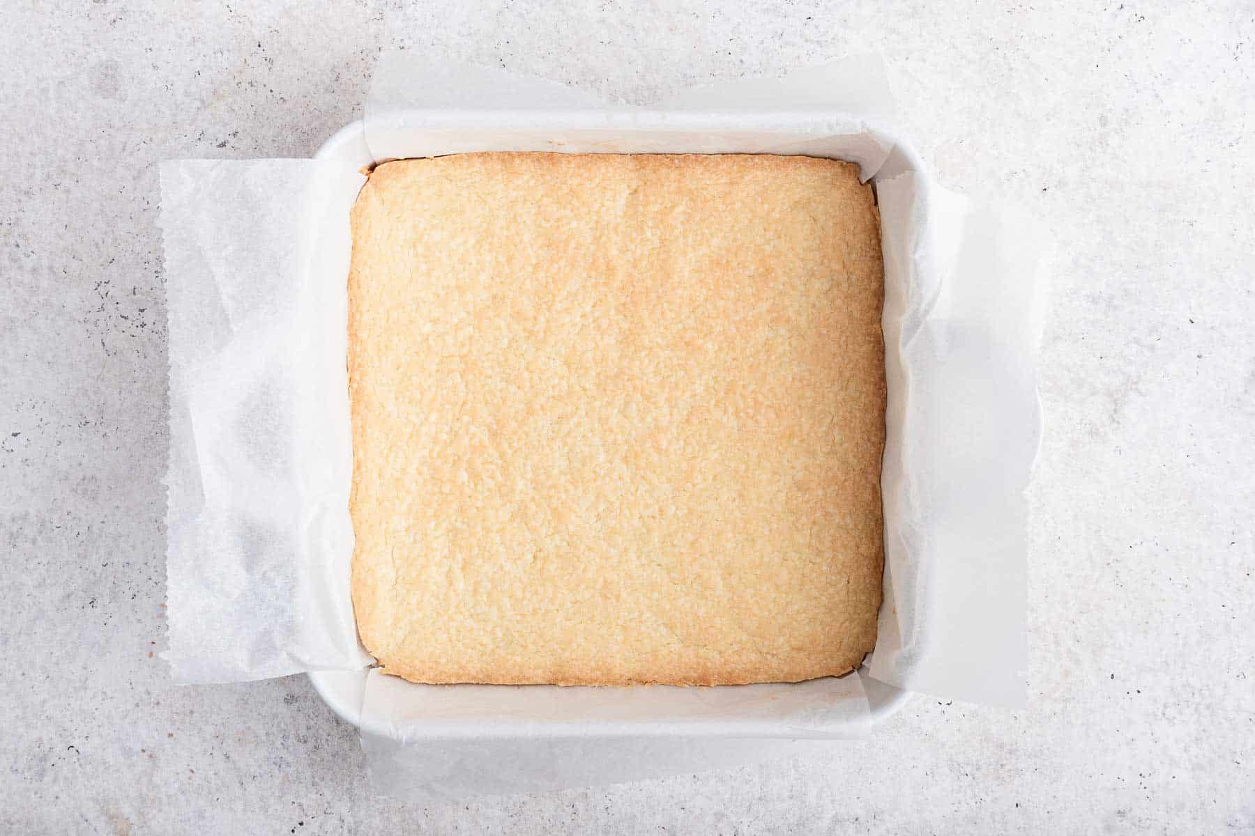 Freshly baked shortbread crust in a square white pan.