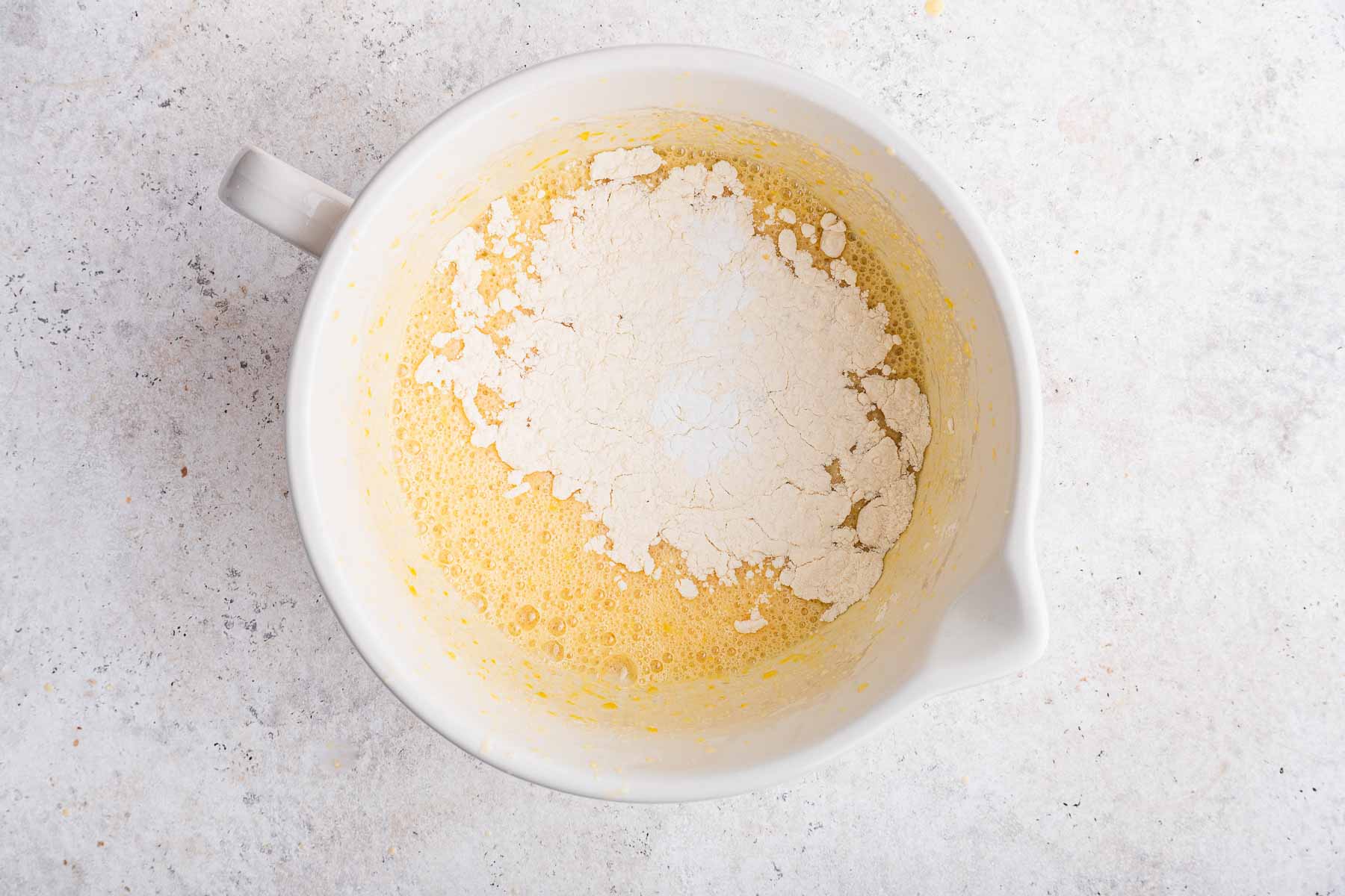 White powder on top of yellow batter in white bowl.