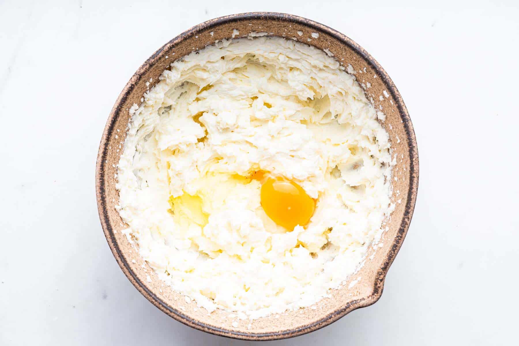 White fluffy batter in brown bowl with egg.