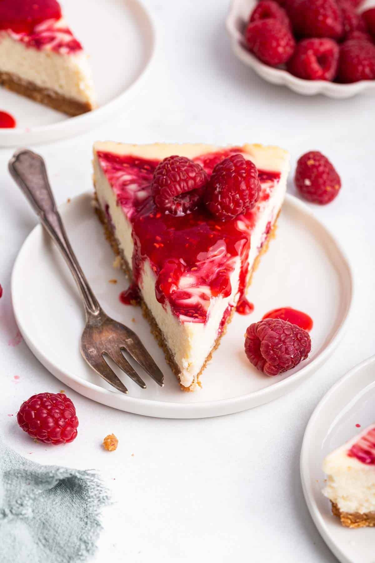 Slice of white chocolate raspberry cheesecake on plate with fork on side.