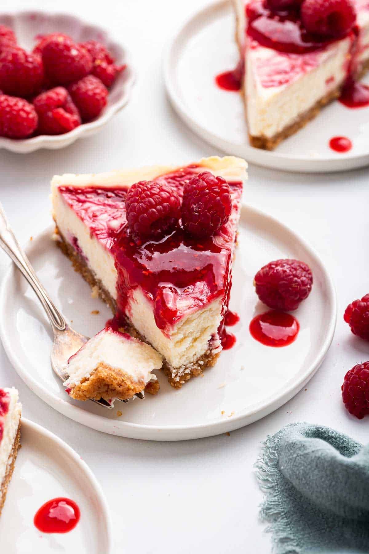 Slice of bright red raspberry white chocolate cheesecake with first bite missing on fork.