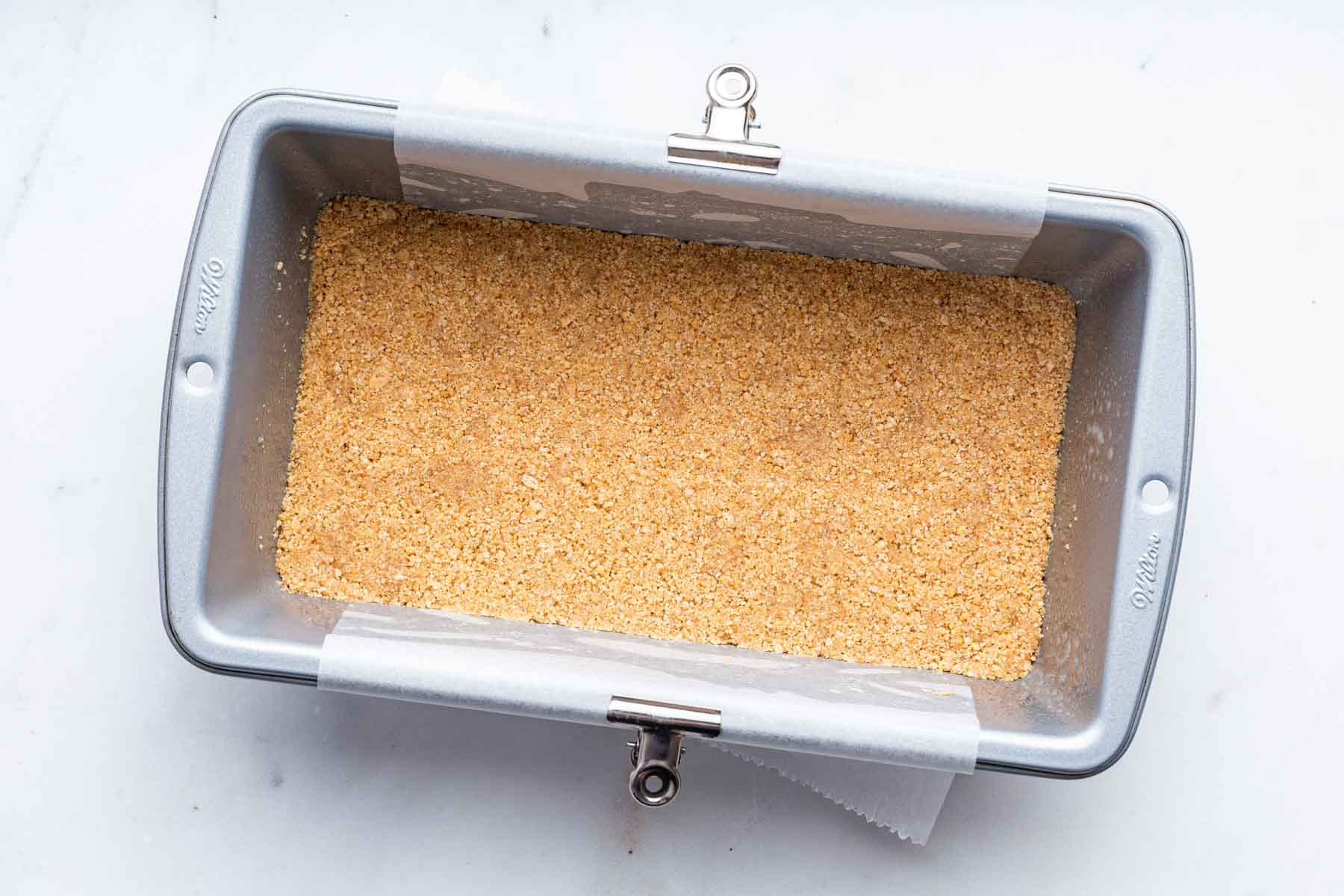Graham cracker crust in a bread loaf pan lined with parchment paper.