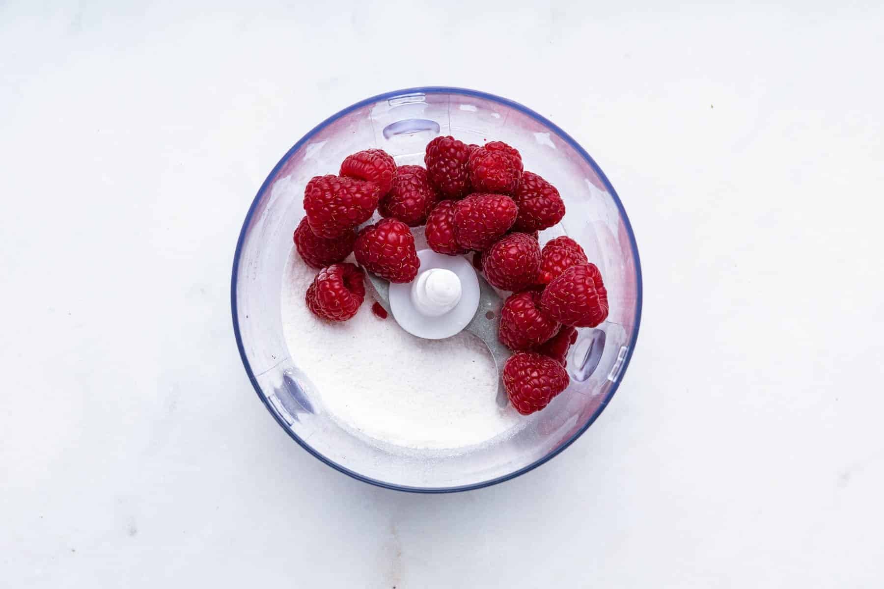 Fresh raspberries and sugar in a mini food processor bowl.
