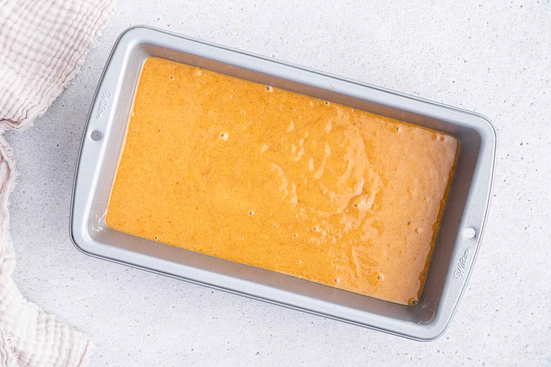 Horizontal image of loaf pan with orange batter, before baking.