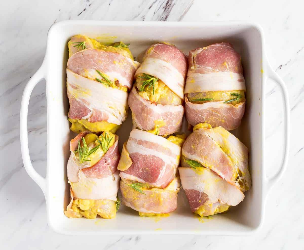 Raw chicken thighs wrapped in bacon and brushed with honey mustard.