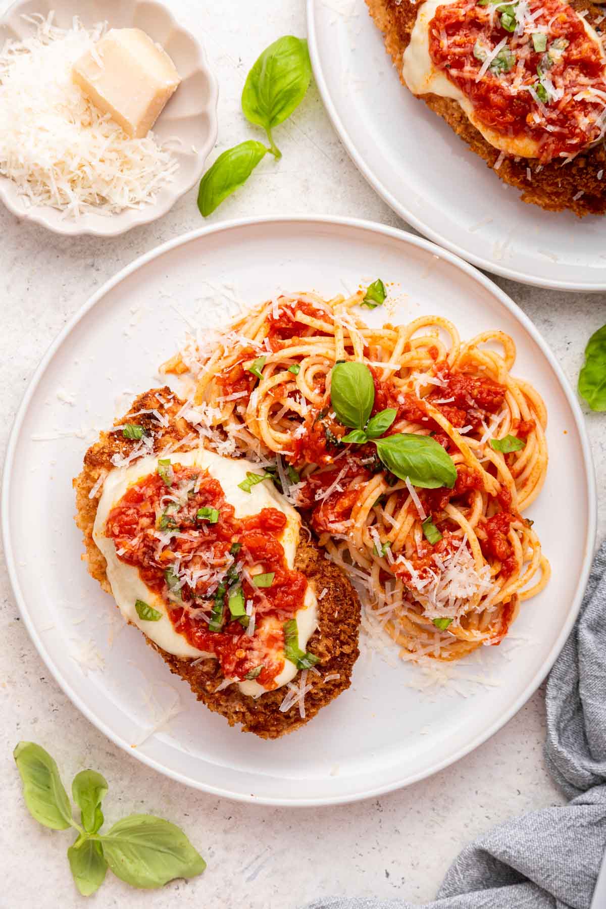 Overhead shot of chicken parmesan on plate with spaghetti noodles and cheese on side.