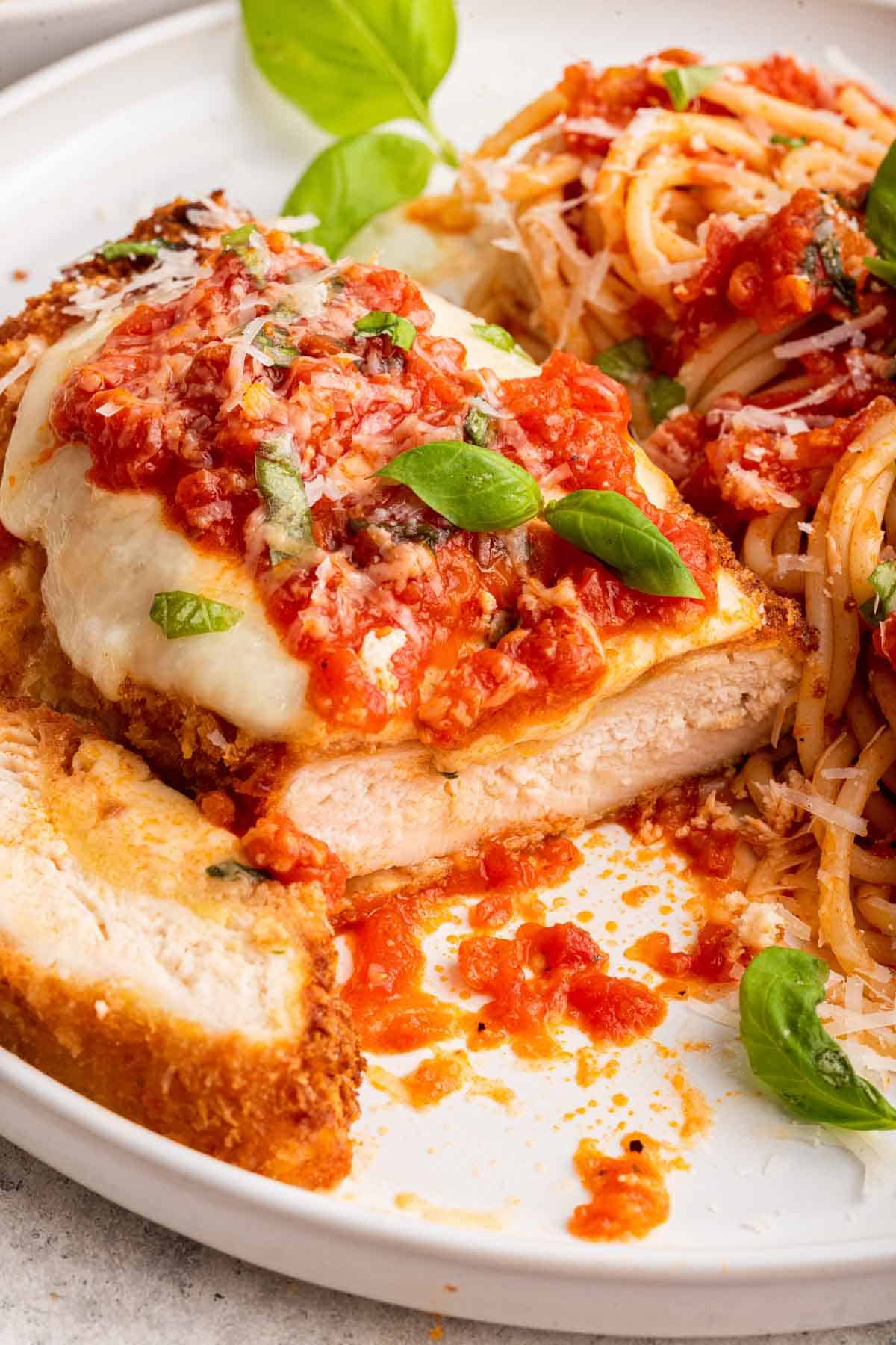 Sliced chicken parmesan on white plate garnished with basil.