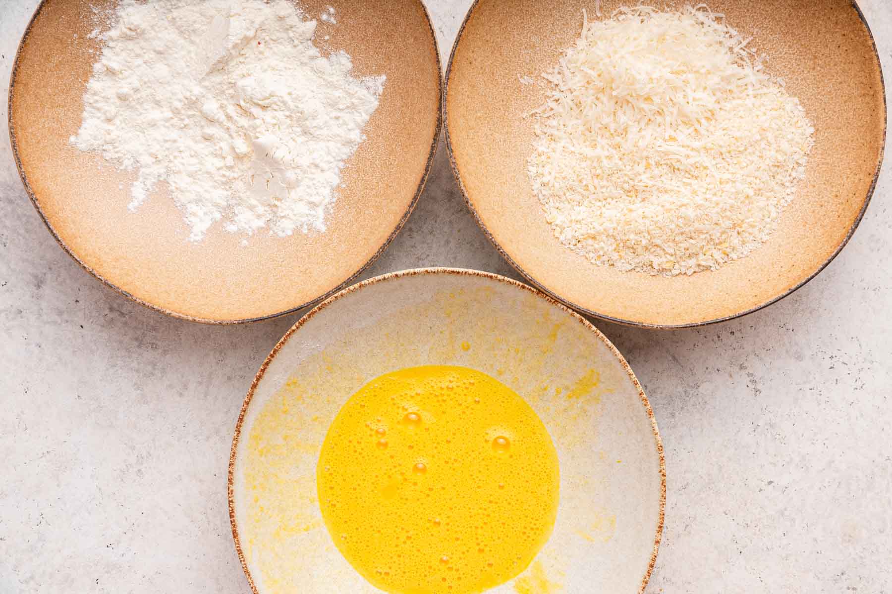 Three bowls with flour, egg and breadcrumbs in each one.