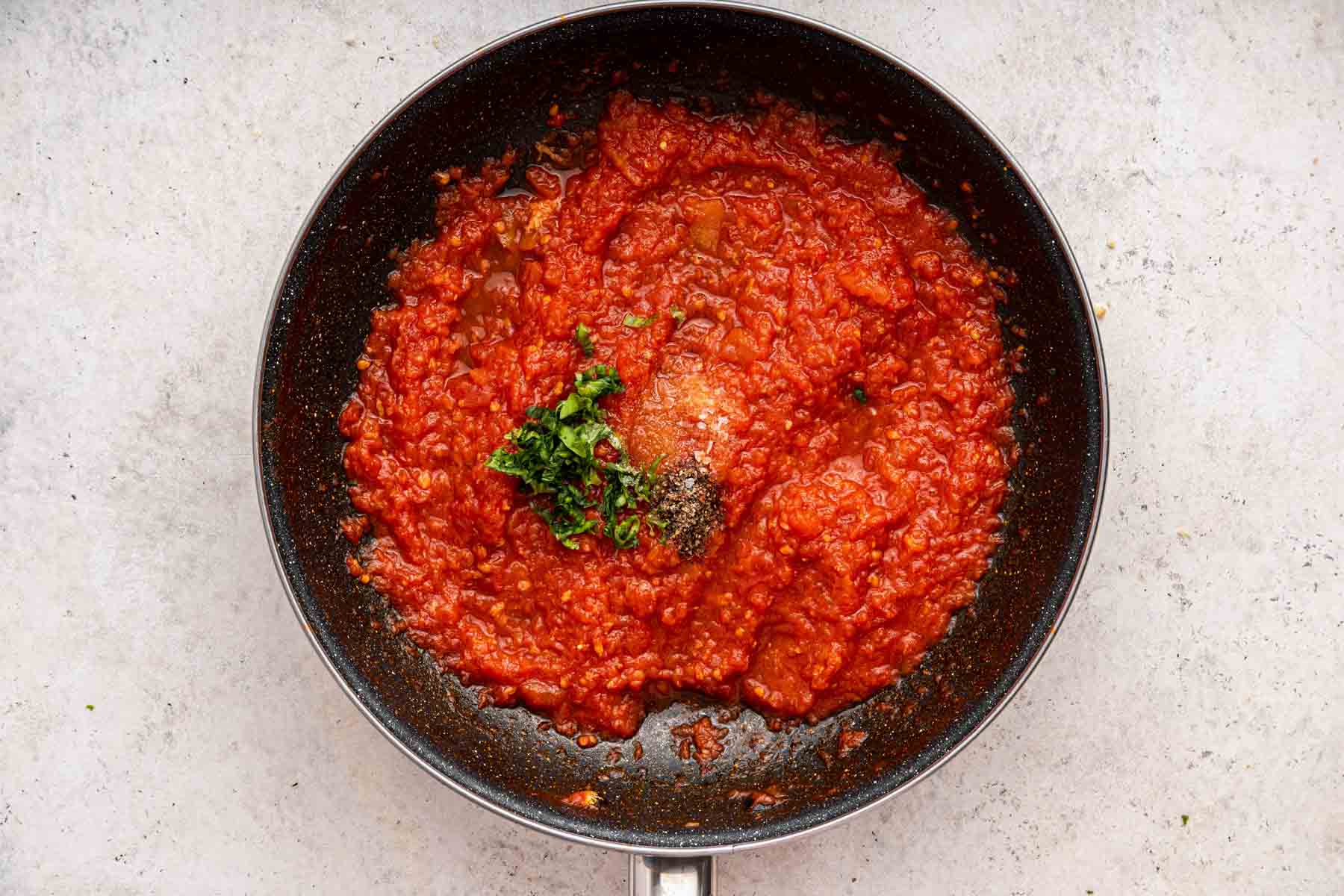 Skillet with bright red tomatoes sauce and fresh herbs in it.