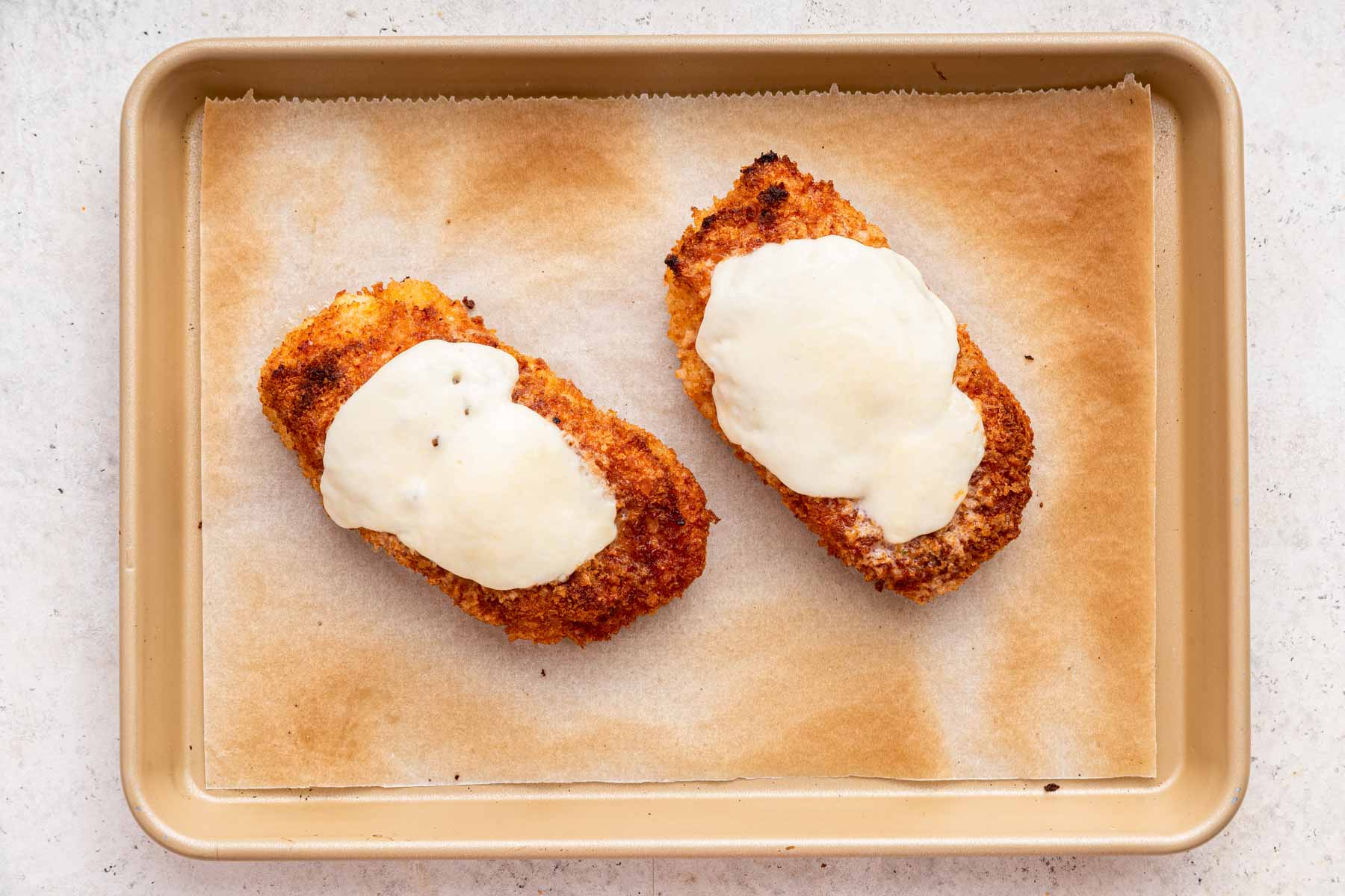 Two rectangular pieces of protein on a baking sheet topped with melted white cheese.