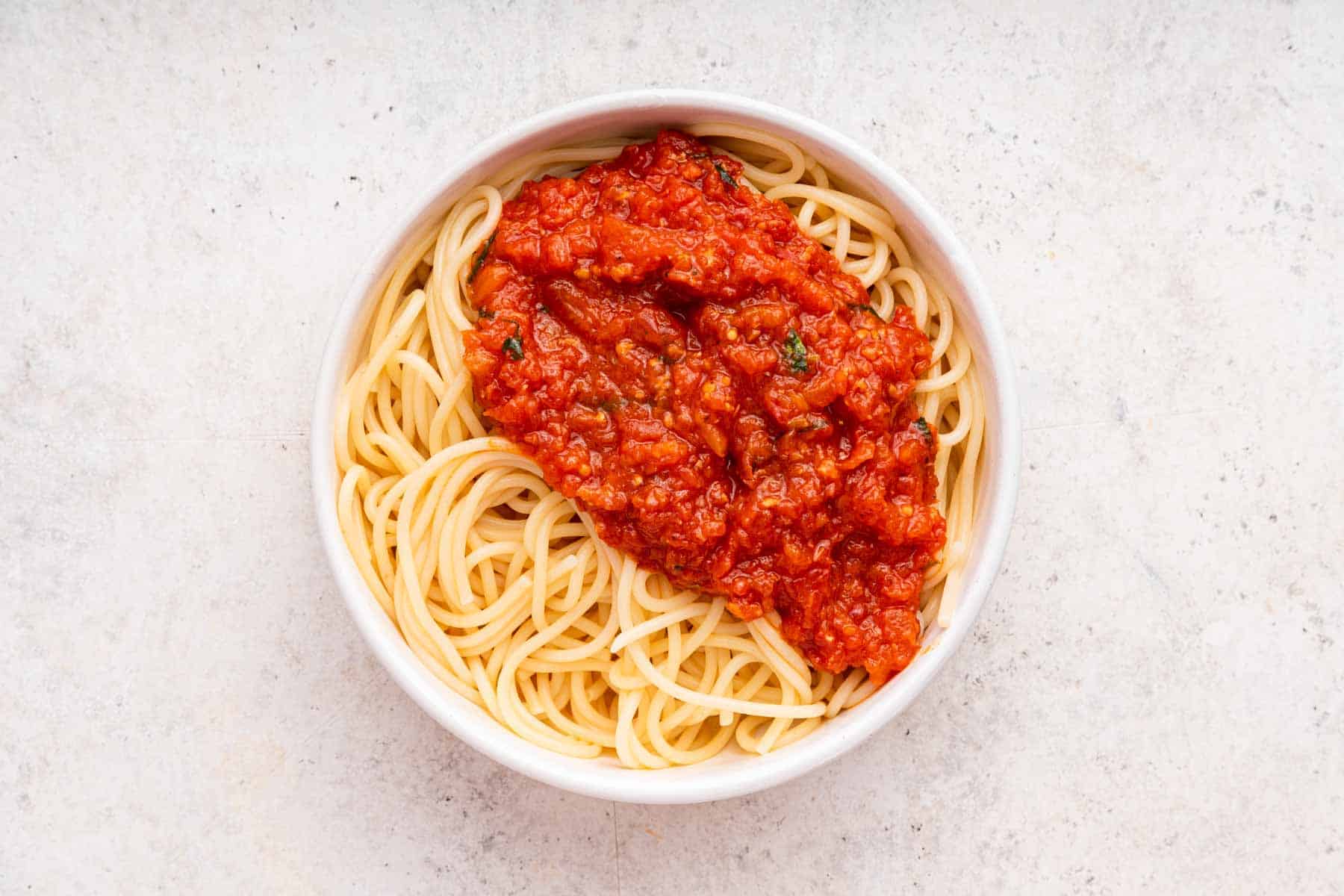 White bowl of spaghetti noodles with tomato sauce poured on top.