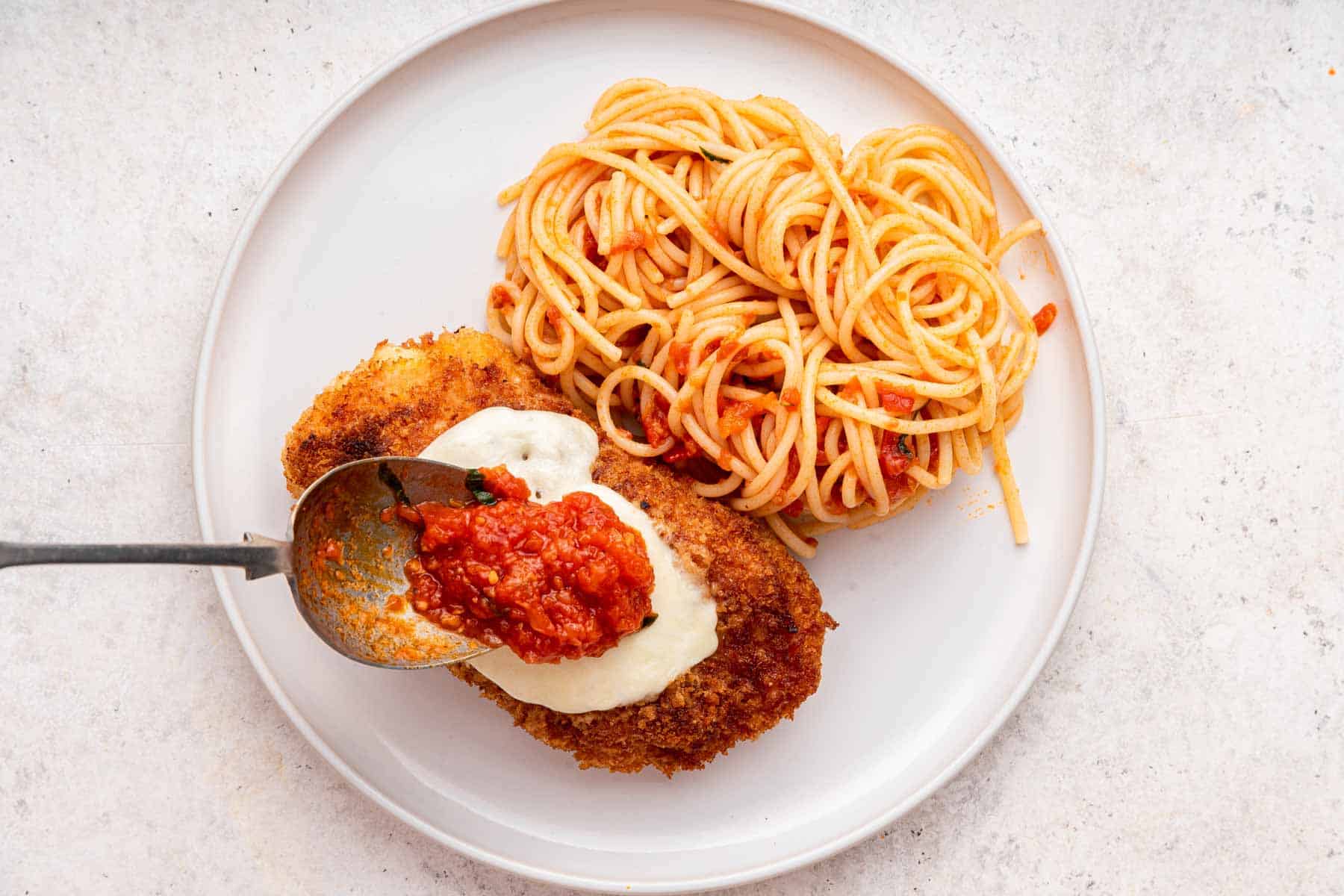 White plate with spaghetti noodles and chicken parmesan on the side.