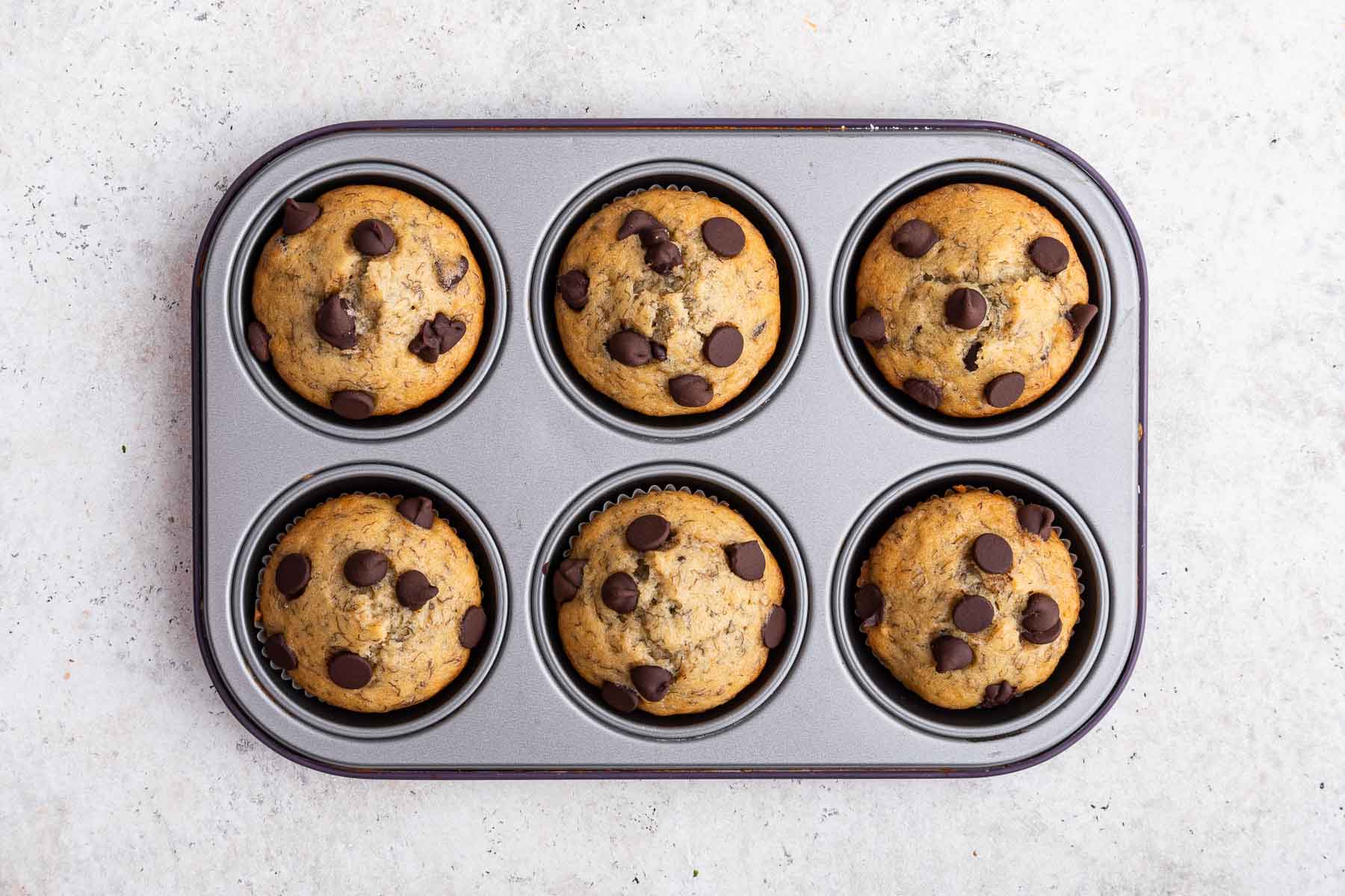 Six freshly baked banana chocolate chip muffins in pan.
