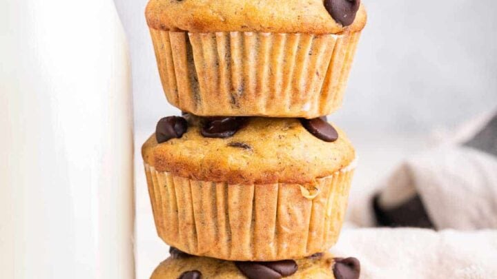 Three chocolate chip banana muffins stacked next to a glass of milk.