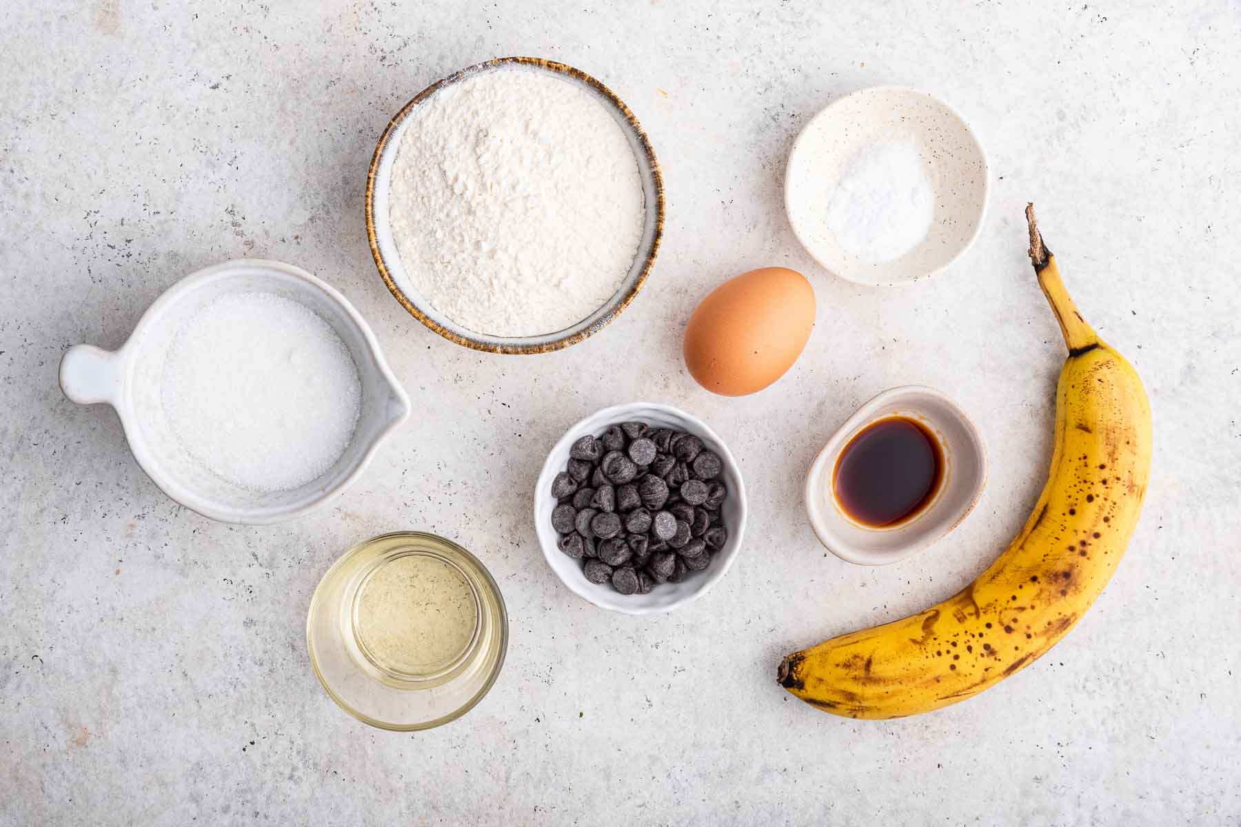 Bowls of flour, sugar, egg and fruit for baking on grey counter.