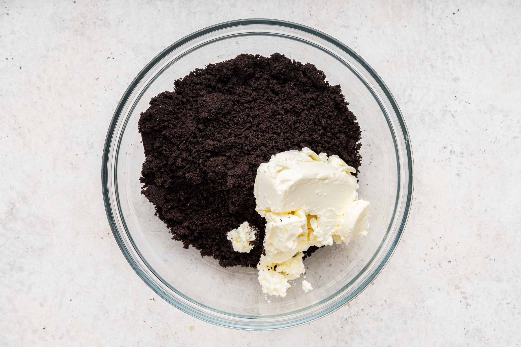 Bowl with crushed black cookies and a scoop of white cream cheese on the side.