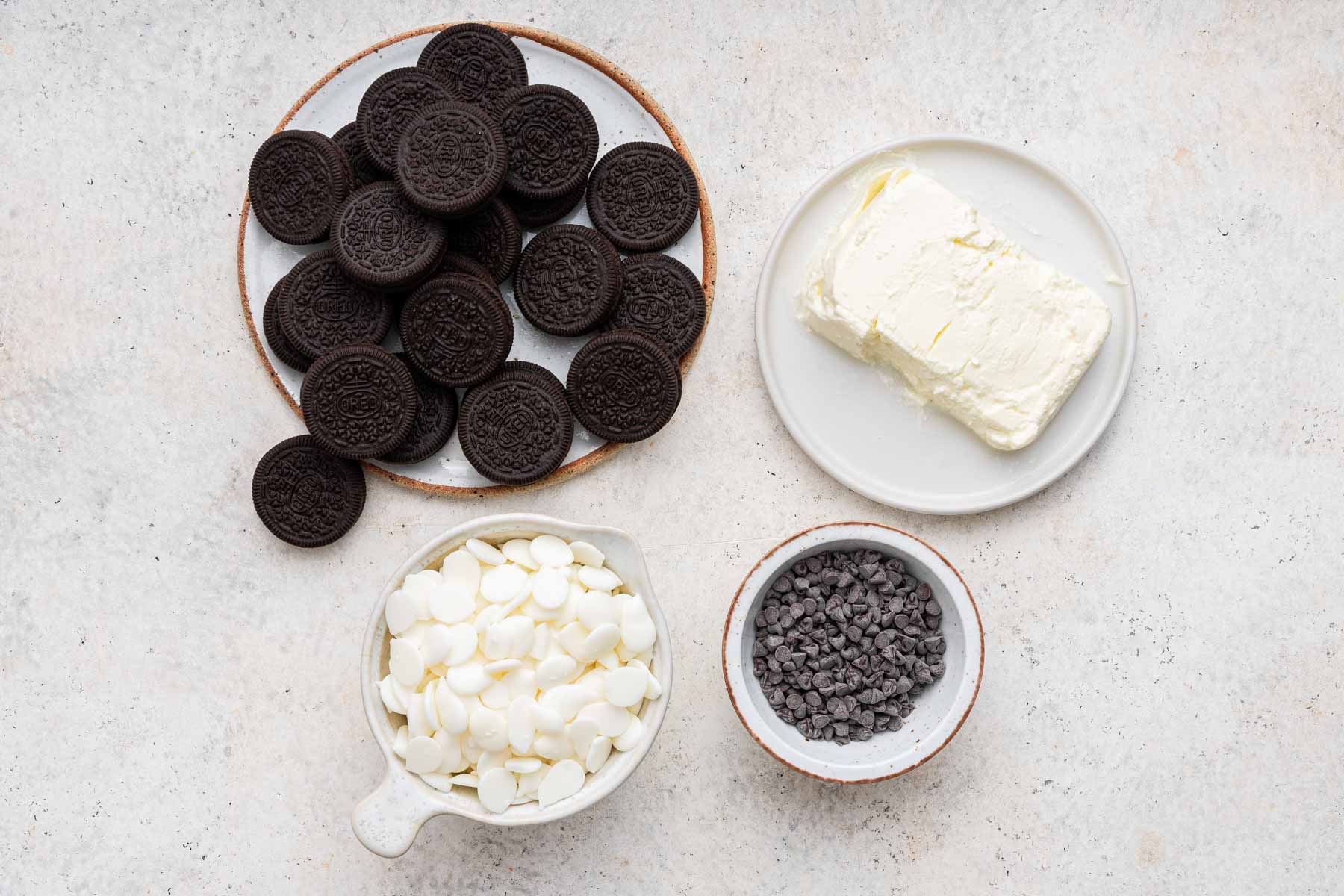 Plate of oreos, white chocolate chips, and cream cheese on grey counter.