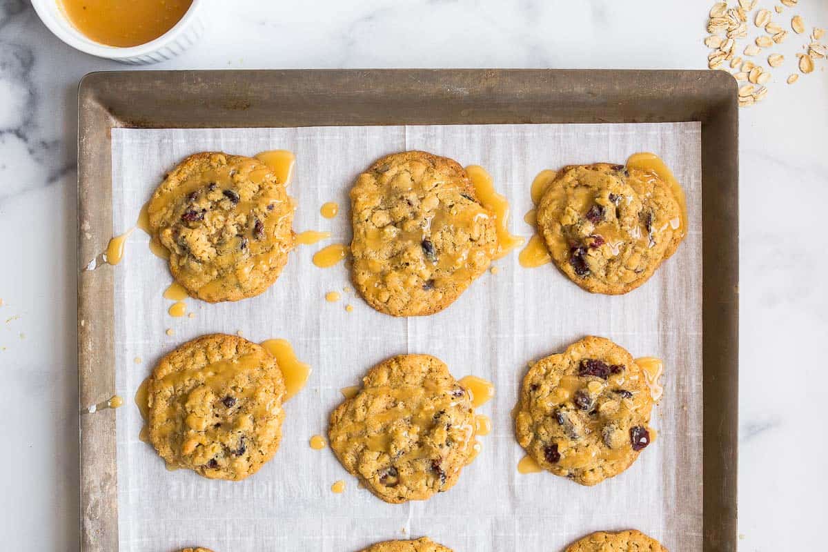 Freshly baked cranberry orange cookies with orange glaze on top on parchment lined baking sheet.