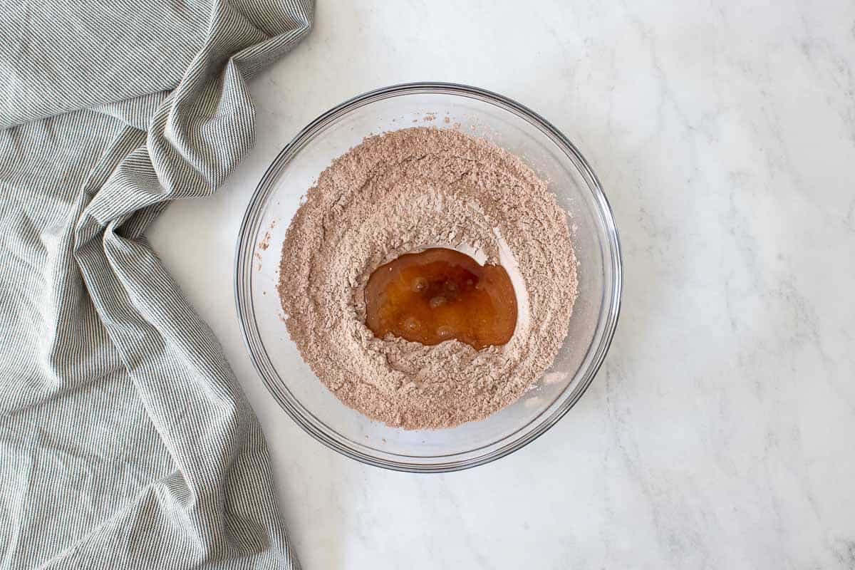 Clear glass bowl with cocoa powder, egg whites and vanilla extract.
